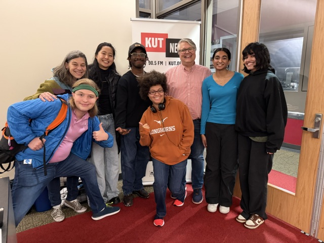 8 people posing together outside a podcast studio at KUTX